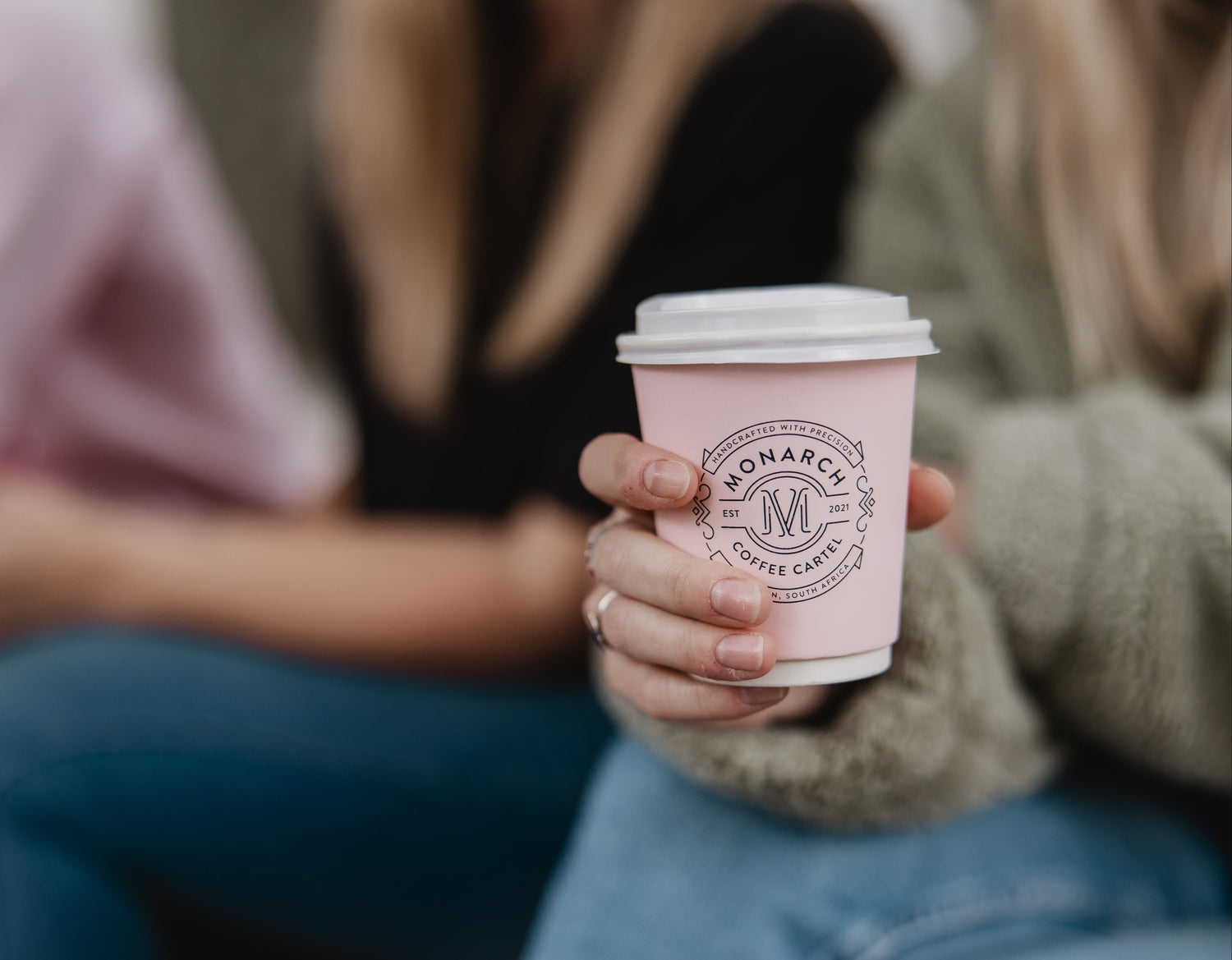 Person holding a pink coffee cup with 'Monarch Coffee' branding.